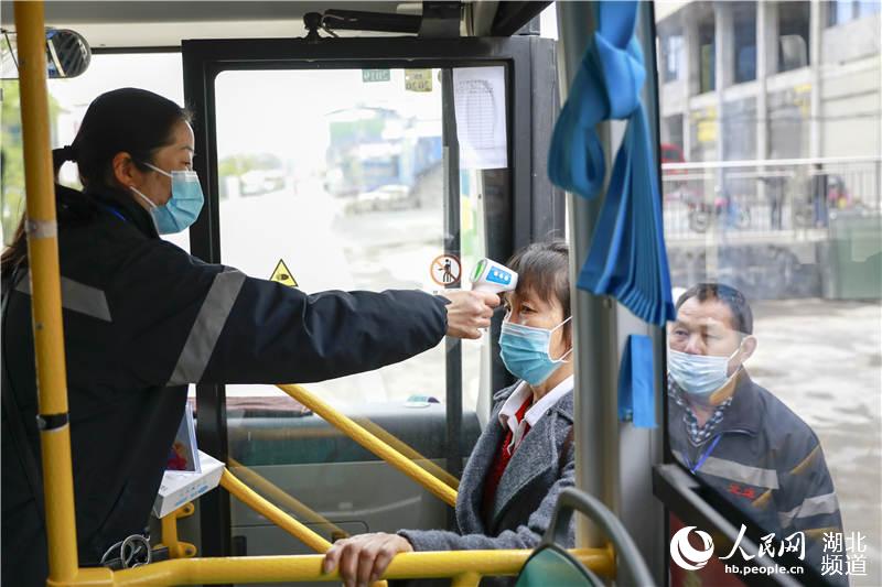 3月28日，在湖南省龍山縣華塘壩中學附近的公交站點，工作人員正給上車乘客檢測體溫。
