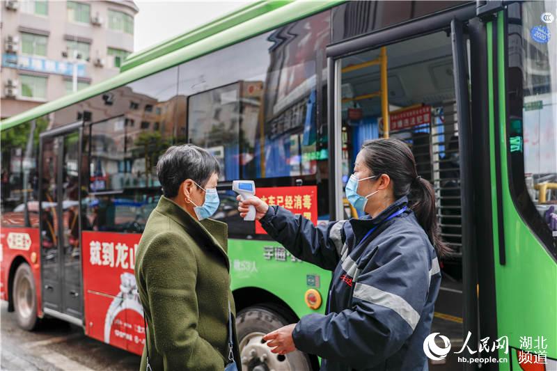 3月28日，在湖北省來鳳縣半邊城公交站點，工作人員正給乘客檢測體溫。
