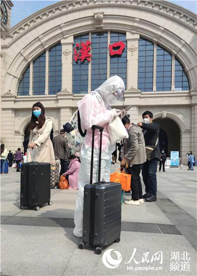 4月8日上午，在漢口火車站站前廣場，旅客們戴囗罩，穿著防護服，在等人排隊進站候車。