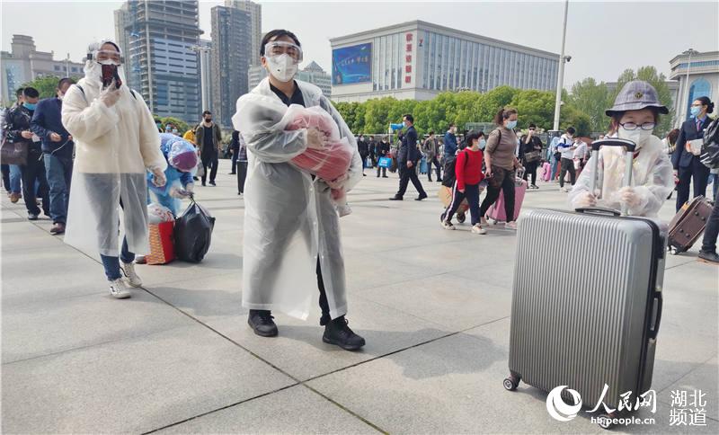 4月8日上午，在漢口火車站站前廣場，這一家人戴囗罩，穿著防護服，保持間距，有序排隊進站候車。