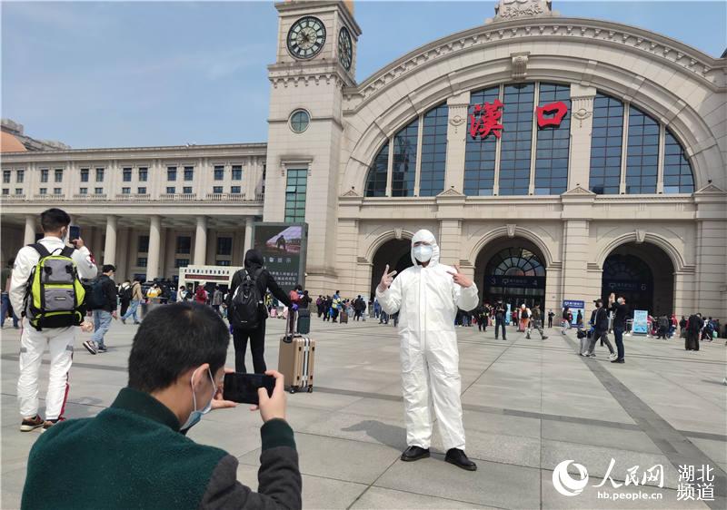 4月8日上午，在漢口火車站站前廣場，一旅客戴囗罩，穿著防護服拍照，留下難忘的歷史瞬間。