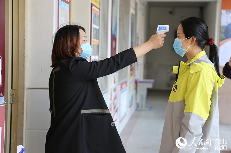 2020年4月27日，湖北省襄陽市保康縣第一中學，參加模擬演練的一名高三年級班主任在教室門口用測溫槍給學生測體溫。
