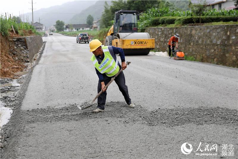 鶴峰縣五裡鄉瓦屋村農村公路改擴建工地上，工人們正冒著風雨、搶抓工期緊張施工。（汪正璽 攝）