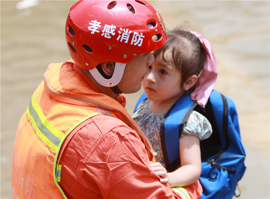 7月24日，在鄭州市中牟縣白沙鎮，湖北孝感消防救援人員幫助1名小女孩涉水。