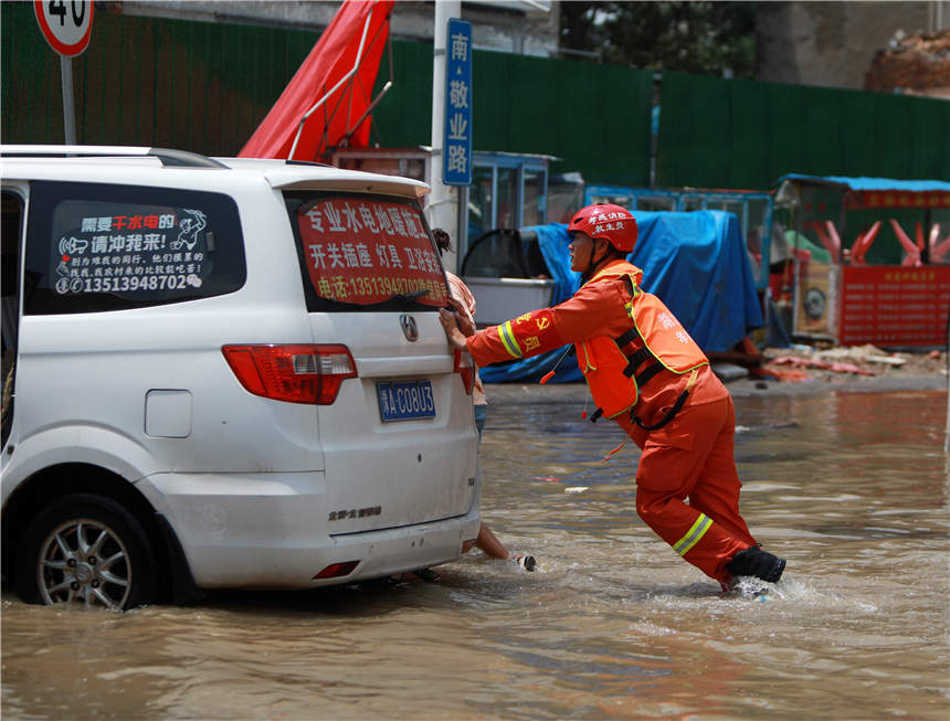 7月24日，在鄭州市中牟縣白沙鎮，湖北孝感消防救援人員正在幫助群眾推車。