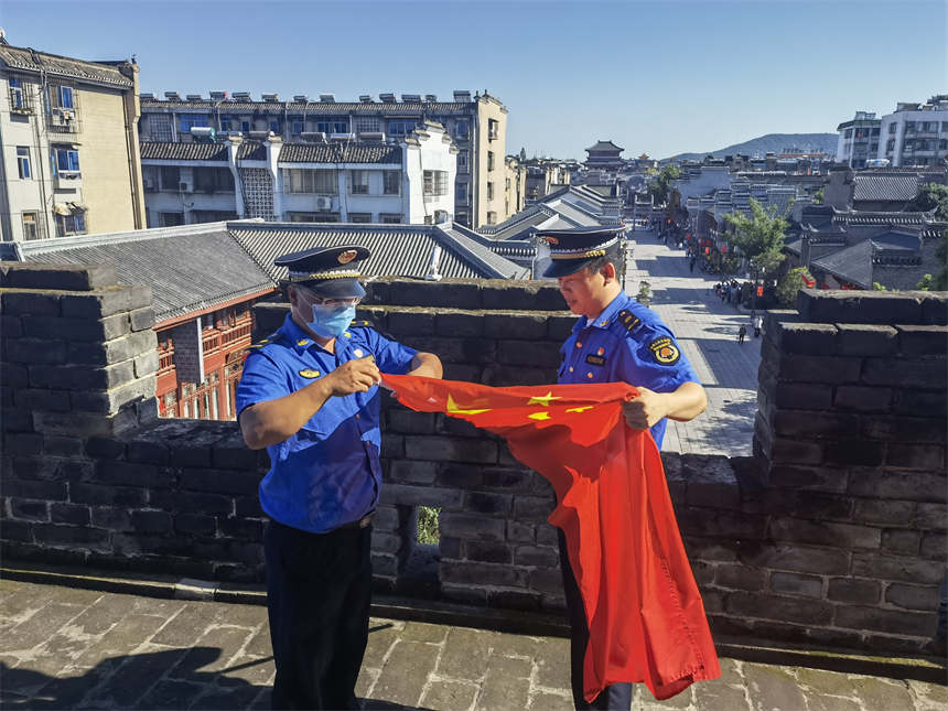 城管執法人員對古城牆上升挂的國旗進行維護