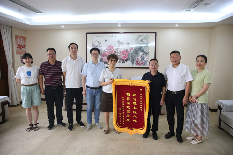 某新能源公司一行来到武汉市生态环境局，将一面绣有“政府服务暖人心，项目落地促发展”的锦旗交到该局一级调研员王杰芳和青山分局局长张勇手中，感谢生态环境部门以热情高效的服务帮助企业项目落地，仅用15工作日就顺利完成环评文件审批。