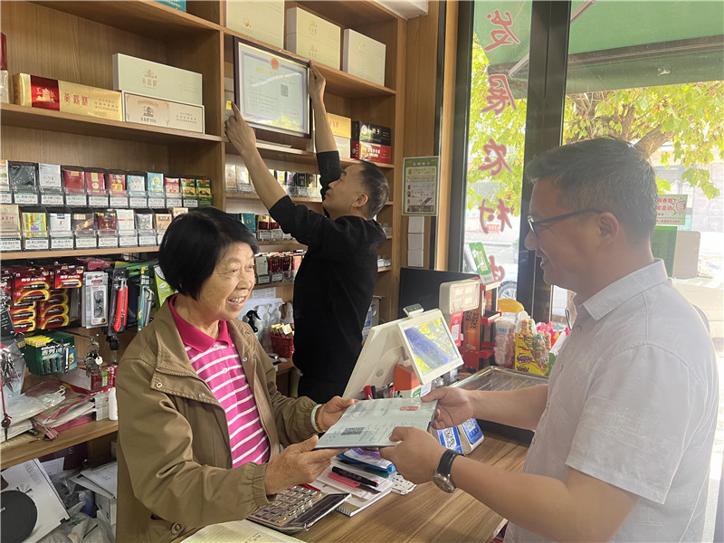 市场“两员”为农网客户王桂华（左）“送证上门”