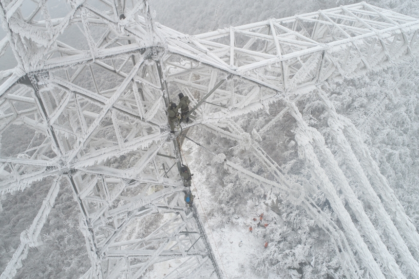 电力应急处置人员爬上70米高的±800千伏陕武输电线路1898号塔，通过机械震动方式清除地线和光缆上的积雪。邹小民摄 