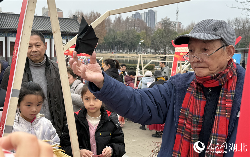 武汉折纸艺术非遗代表性传承人李星旺老人向大家展示会“飞”的蝙蝠。人民网记者 周恬摄