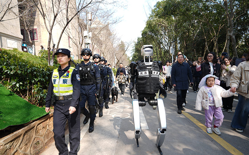武汉大学樱花大道上，一台身着黑色马甲的白色人形机器人穿梭在赏樱人群，科技感十足的执勤现场秒变沉浸式体验未来警务的“露天课堂”。