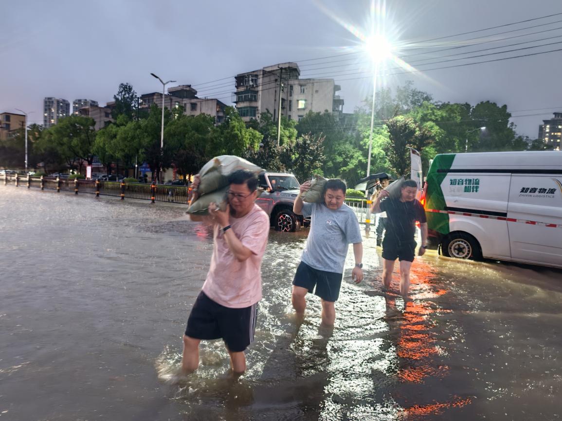 救援小組成員蹚水為受災路段零售戶運送沙袋。陳麗群攝