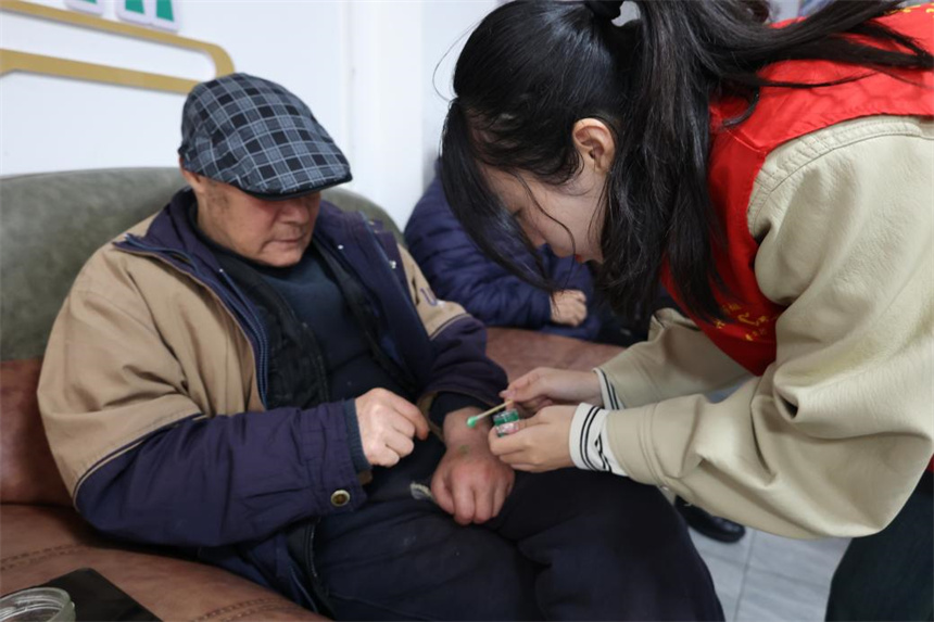 志愿者邱凯欣（右）为老人上药。